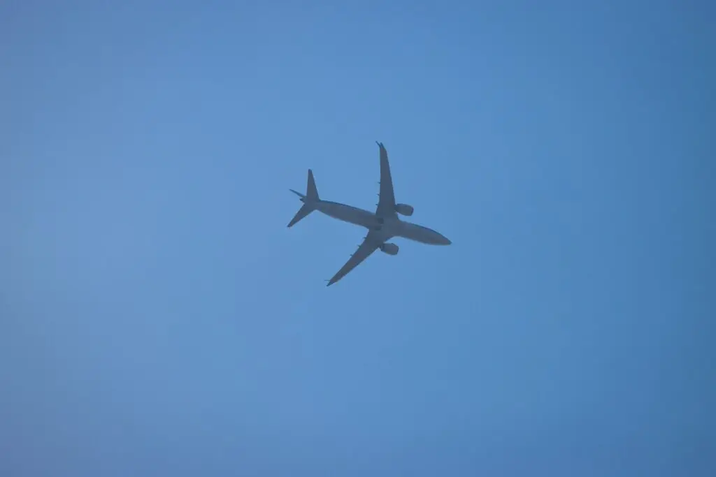 Silhouette of an airplane in flight over Corfu, Greece, with a clear blue sky background.