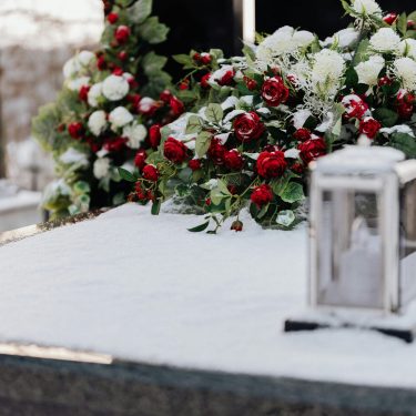 Grave adorned with roses and chrysanthemums in winter snow, evoking solemnity and remembrance.